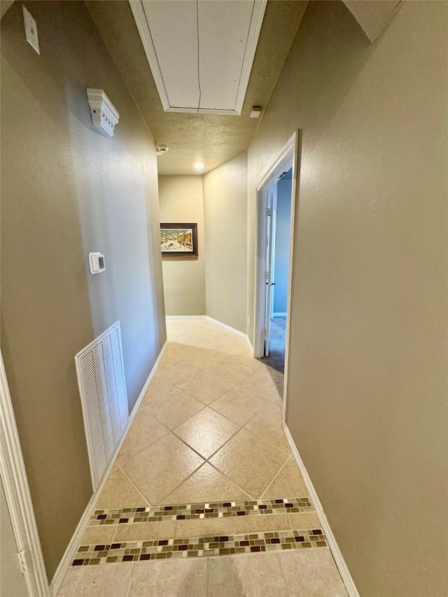 hall with baseboards, tile patterned flooring, visible vents, and attic access