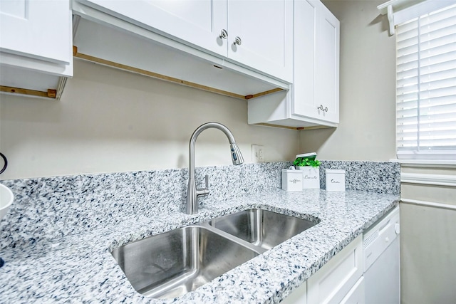 kitchen with white dishwasher, light stone countertops, sink, and white cabinets