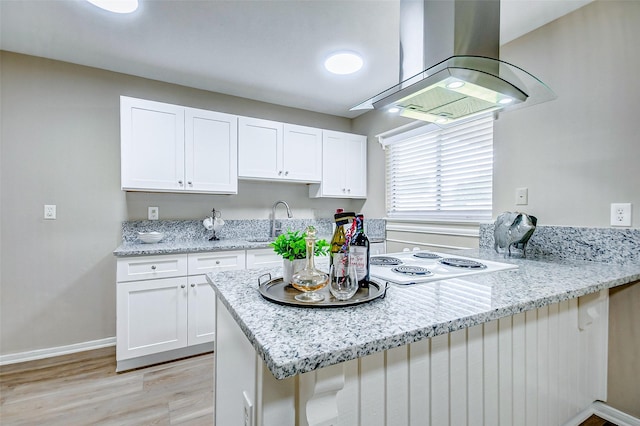 kitchen featuring island range hood, light wood-type flooring, kitchen peninsula, light stone countertops, and white cabinets