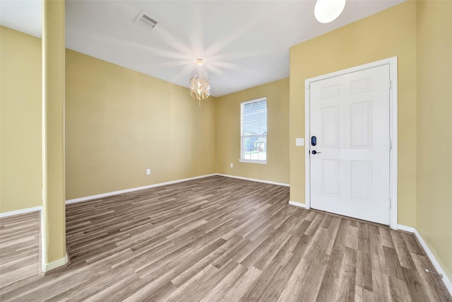 foyer featuring an inviting chandelier, wood finished floors, visible vents, and baseboards