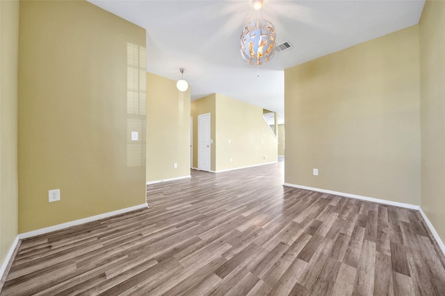 empty room with a notable chandelier, wood finished floors, visible vents, and baseboards