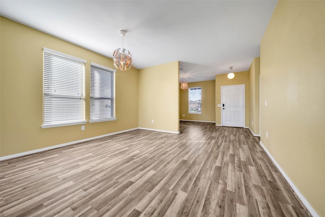 empty room featuring light wood finished floors, baseboards, and a chandelier