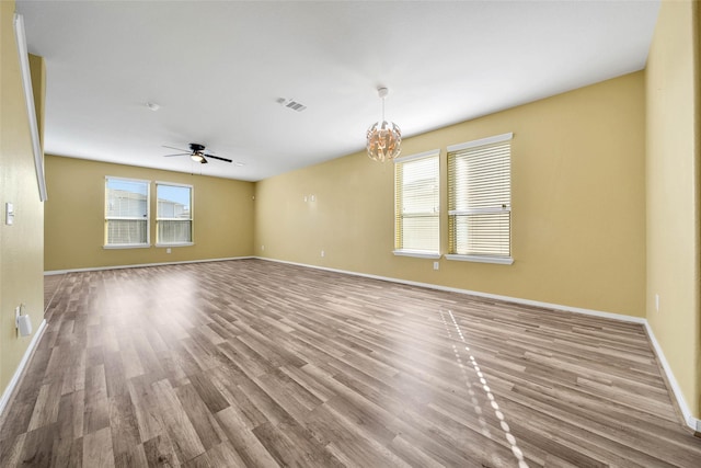 spare room featuring light wood-type flooring, visible vents, baseboards, and ceiling fan with notable chandelier