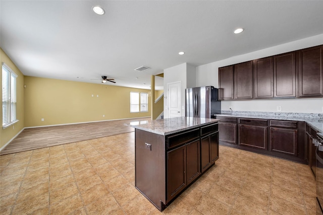 kitchen featuring dark brown cabinetry, a healthy amount of sunlight, a center island, and stainless steel refrigerator