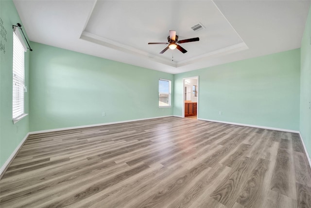 empty room with light wood finished floors, baseboards, and a tray ceiling