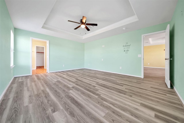 unfurnished bedroom featuring ceiling fan, a spacious closet, a raised ceiling, and light wood-type flooring