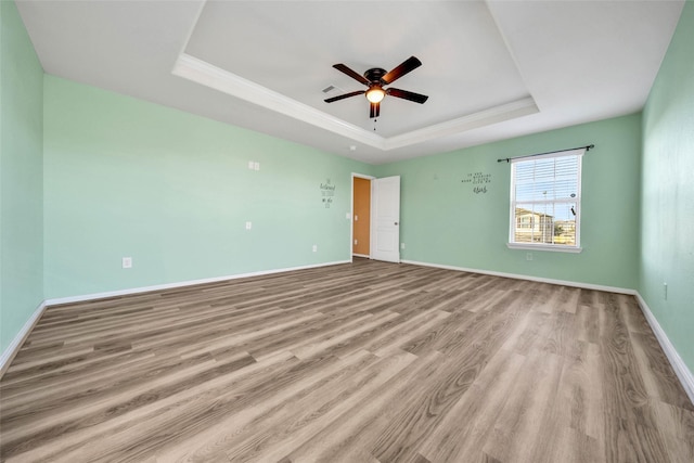 spare room with a raised ceiling, baseboards, ceiling fan, and light wood finished floors