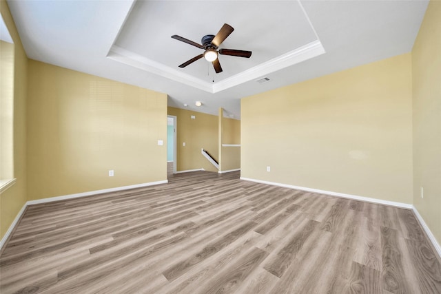 empty room with visible vents, a tray ceiling, light wood-style flooring, and baseboards