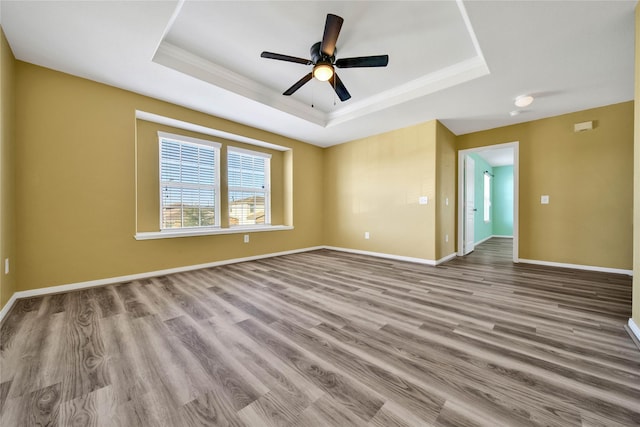 empty room with a ceiling fan, light wood-type flooring, a raised ceiling, and baseboards