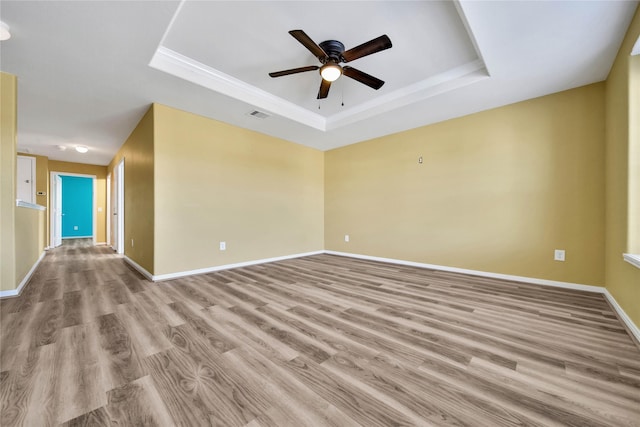 spare room featuring a raised ceiling, visible vents, a ceiling fan, light wood-type flooring, and baseboards