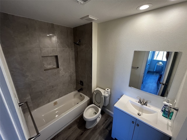 full bathroom with hardwood / wood-style flooring, tiled shower / bath, vanity, and toilet