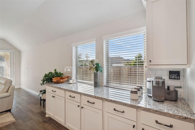 kitchen with tasteful backsplash, white cabinetry, vaulted ceiling, and light stone countertops