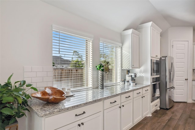 kitchen with dark wood-type flooring, light stone counters, vaulted ceiling, appliances with stainless steel finishes, and white cabinets