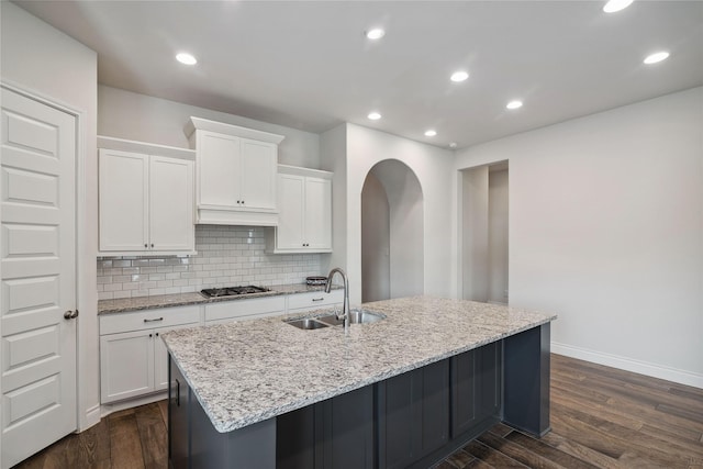 kitchen with sink, dark wood-type flooring, white cabinetry, stainless steel gas cooktop, and a center island with sink