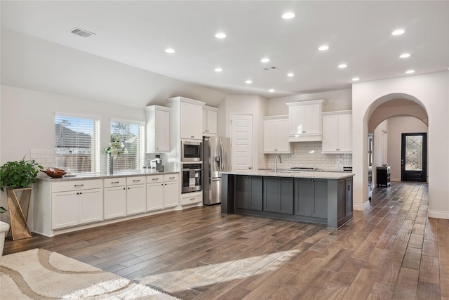 kitchen with appliances with stainless steel finishes, tasteful backsplash, white cabinets, a kitchen island with sink, and light stone counters