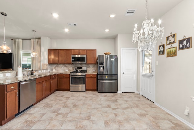 kitchen featuring hanging light fixtures, stainless steel appliances, tasteful backsplash, a wealth of natural light, and light stone countertops