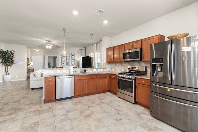 kitchen with hanging light fixtures, stainless steel appliances, kitchen peninsula, and light stone countertops