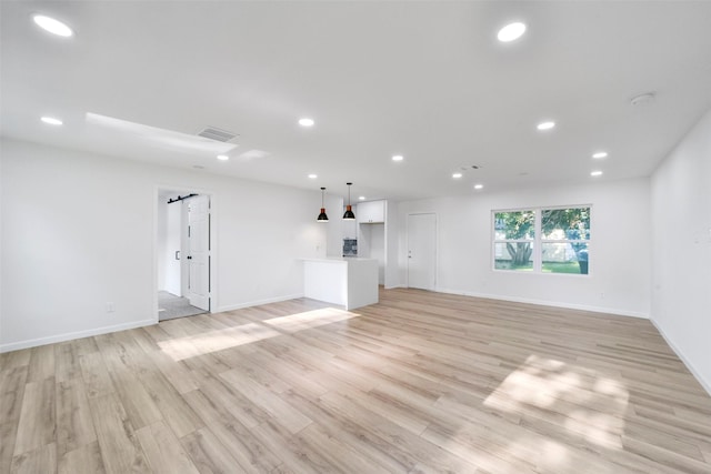 unfurnished living room featuring a barn door and light wood-type flooring