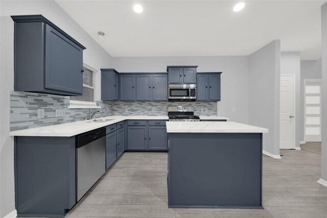 kitchen with appliances with stainless steel finishes, tasteful backsplash, sink, a center island, and light stone counters