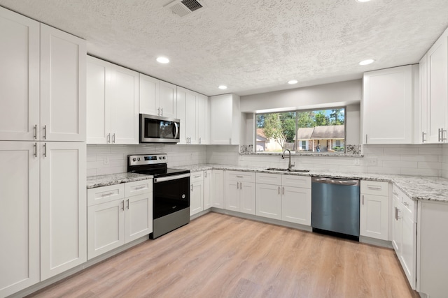 kitchen featuring sink, appliances with stainless steel finishes, white cabinetry, light stone counters, and light hardwood / wood-style floors