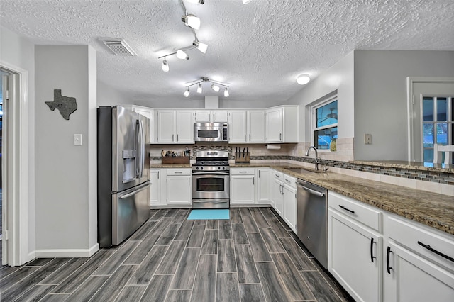 kitchen featuring appliances with stainless steel finishes, tasteful backsplash, white cabinetry, sink, and dark stone counters