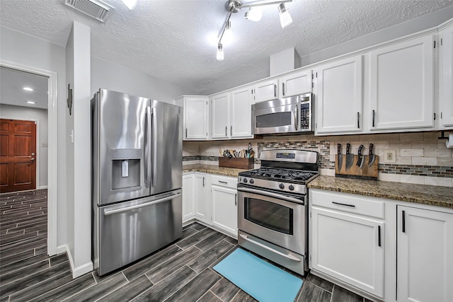 kitchen with white cabinetry, tasteful backsplash, dark stone counters, and appliances with stainless steel finishes