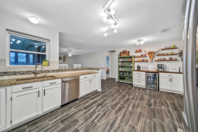 kitchen featuring sink, stainless steel dishwasher, dark stone counters, beverage cooler, and white cabinets