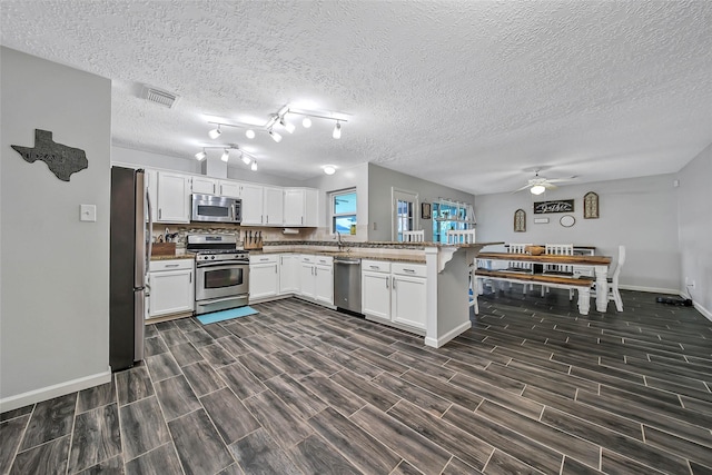 kitchen featuring appliances with stainless steel finishes, white cabinetry, sink, ceiling fan, and kitchen peninsula