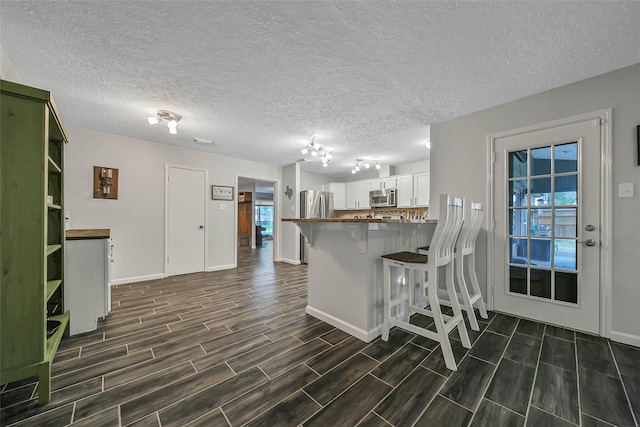 kitchen featuring a breakfast bar area, appliances with stainless steel finishes, a textured ceiling, white cabinets, and kitchen peninsula