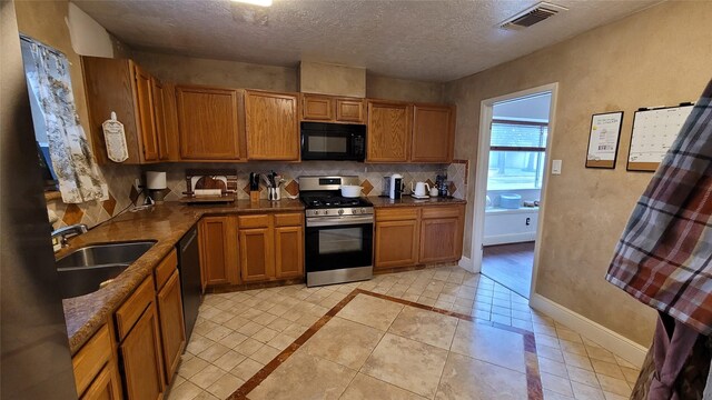 kitchen with sink, a textured ceiling, light tile patterned floors, decorative backsplash, and black appliances