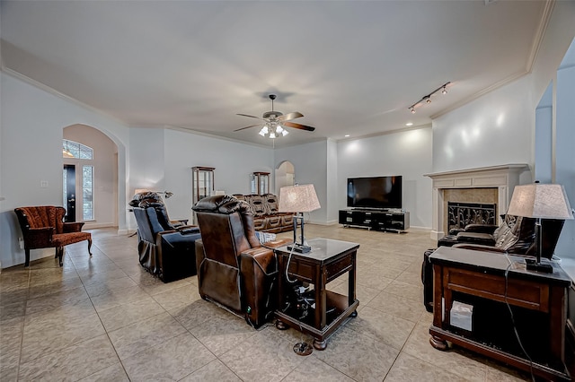 living area featuring light tile patterned floors, arched walkways, a ceiling fan, a tile fireplace, and ornamental molding