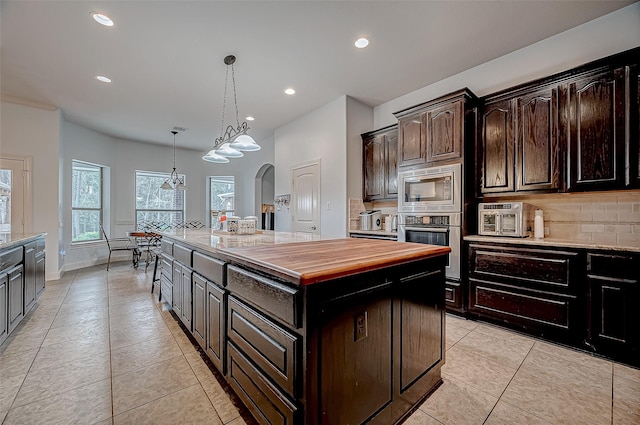 kitchen with arched walkways, pendant lighting, appliances with stainless steel finishes, a kitchen island, and dark brown cabinetry