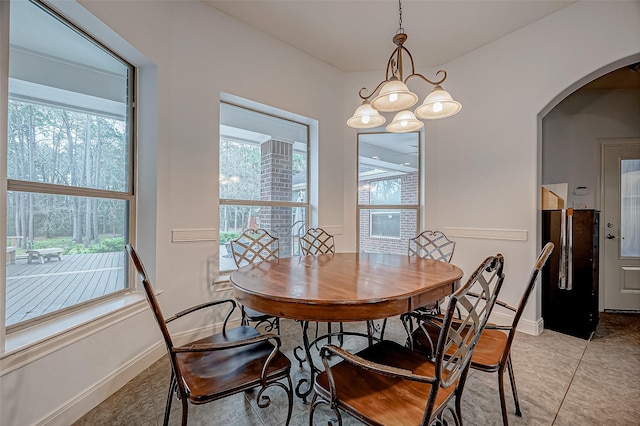 dining room featuring a healthy amount of sunlight, light tile patterned floors, baseboards, and arched walkways