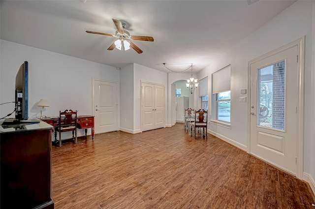 living area with ceiling fan with notable chandelier, arched walkways, baseboards, and wood finished floors