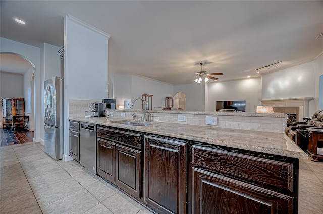 kitchen featuring arched walkways, stainless steel appliances, backsplash, a sink, and dark brown cabinets