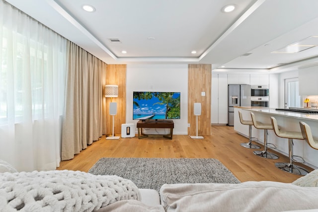 living room with a tray ceiling and light wood-type flooring