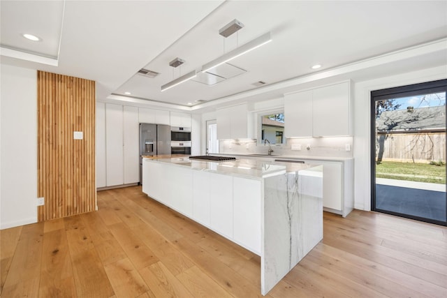 kitchen with pendant lighting, sink, light hardwood / wood-style floors, white cabinets, and a kitchen island