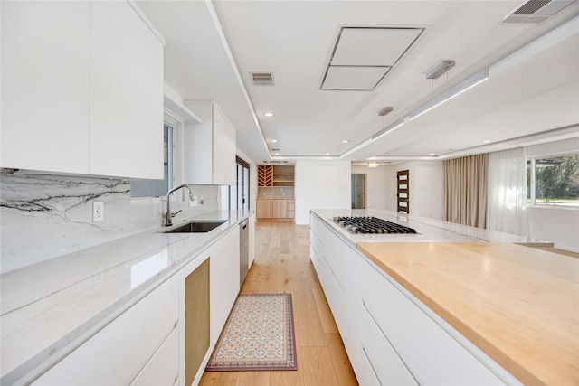 kitchen featuring white cabinetry, sink, decorative backsplash, light stone counters, and light hardwood / wood-style floors