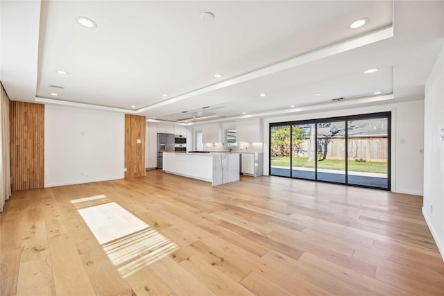 unfurnished living room featuring a raised ceiling and light hardwood / wood-style floors