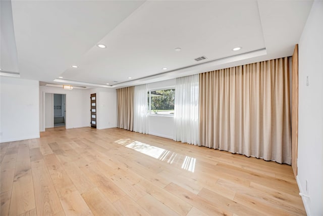 spare room featuring light wood-type flooring and a tray ceiling