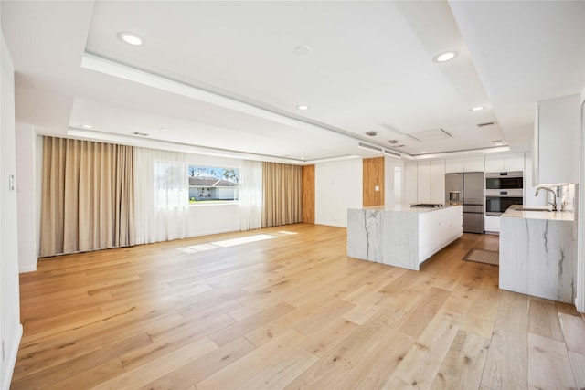 kitchen with sink, appliances with stainless steel finishes, a tray ceiling, light hardwood / wood-style floors, and white cabinets