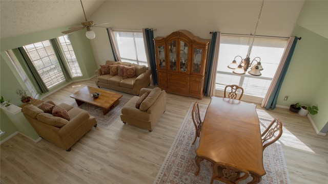 living room featuring high vaulted ceiling, ceiling fan with notable chandelier, and light wood-type flooring