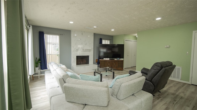 living room with a premium fireplace, a textured ceiling, and light wood-type flooring