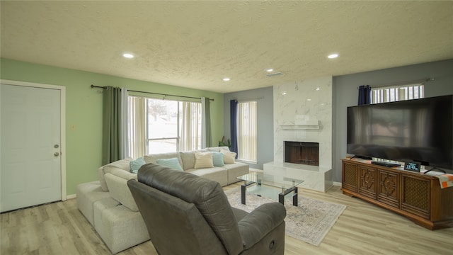 living room with a textured ceiling, a high end fireplace, and light hardwood / wood-style flooring