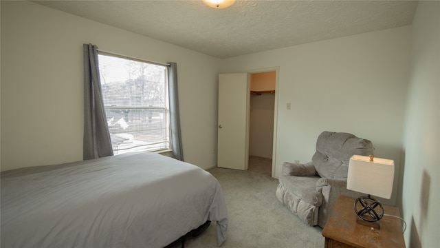 bedroom with a spacious closet, light colored carpet, and a textured ceiling