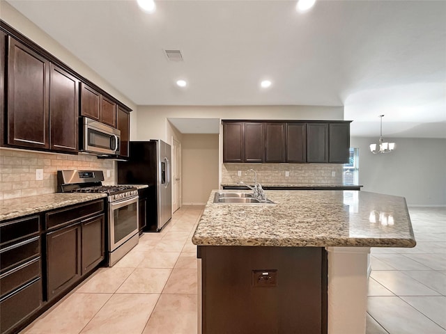 kitchen with appliances with stainless steel finishes, pendant lighting, an island with sink, sink, and dark brown cabinets