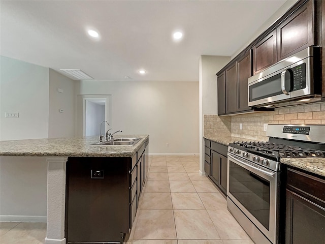 kitchen with sink, appliances with stainless steel finishes, backsplash, dark brown cabinets, and an island with sink