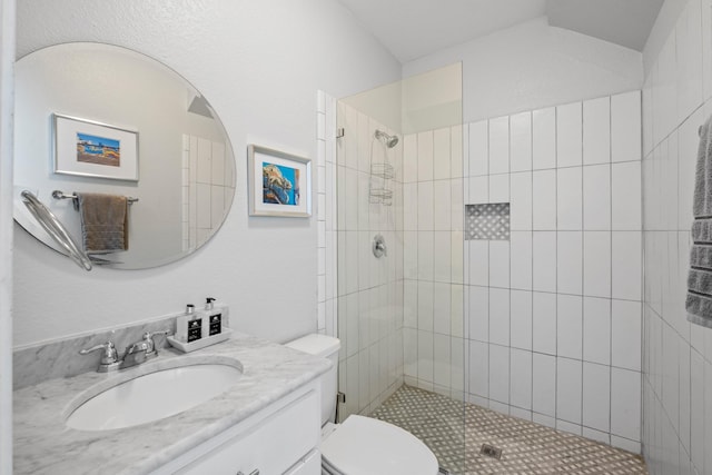 bathroom featuring tiled shower, vanity, toilet, and vaulted ceiling