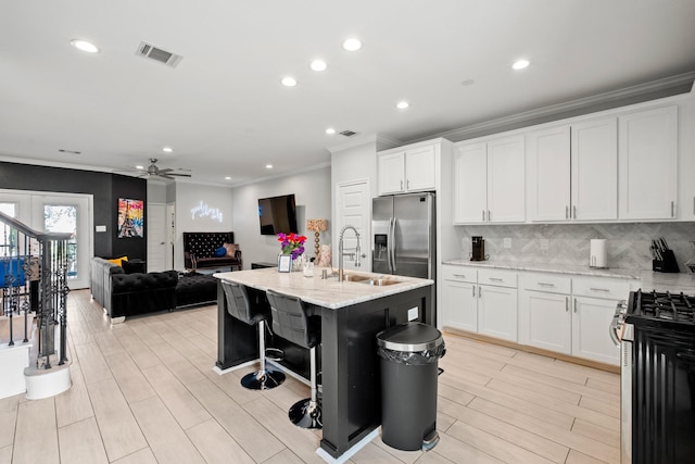 kitchen with sink, appliances with stainless steel finishes, light stone countertops, white cabinets, and a center island with sink