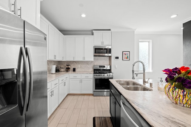 kitchen with sink, crown molding, appliances with stainless steel finishes, white cabinetry, and light stone counters